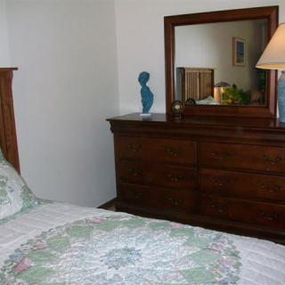 A cozy bedroom with a wooden dresser, mirror, and a bed adorned with a quilt.