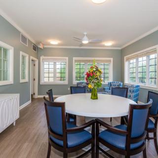 A well-lit dining room featuring a round table with chairs and a floral centerpiece.