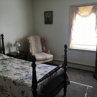 A traditionally decorated bedroom with a single bed, an armchair, and a window with drapes.