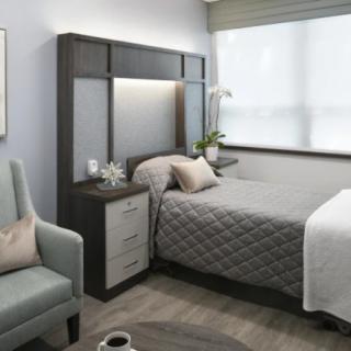 A modern bedroom with a gray quilted bed, bedside table, and an armchair near a large window.