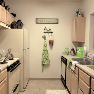 A cozy kitchen with light wooden cabinets, decorated with green accents and a neatly hung apron.