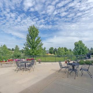 A spacious outdoor patio with tables and chairs, surrounded by lush greenery and a partly cloudy sky.
