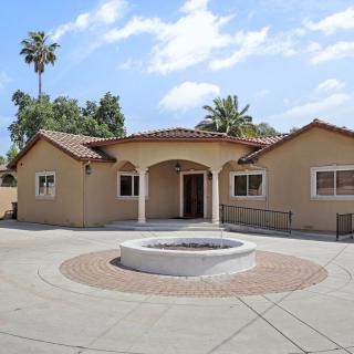 A beige residential house with a fountain in the front yard and palm trees surrounding the property.