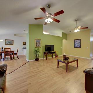 A spacious open-plan living and dining area with wooden flooring, featuring ceiling fans, a TV, and a green accent wall.
