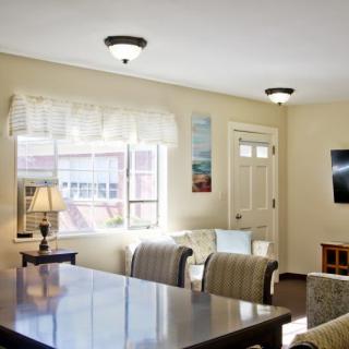 A bright living room featuring a table, comfortable chairs, a television, and a window with natural light.