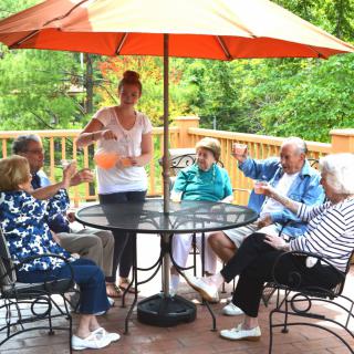 A group of people sitting around a table with an umbrella, enjoying a conversation outdoors on a deck.