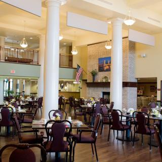 A spacious and elegantly designed dining area with multiple tables and chairs, featuring large columns and a warm atmosphere.
