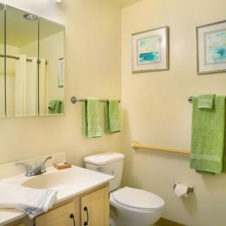 A clean and organized bathroom with green towels and wall art.