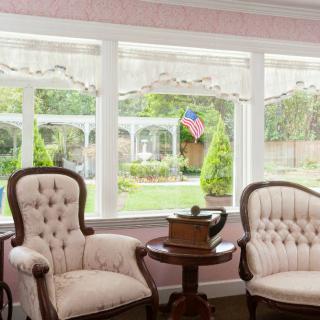 A cozy sitting area with antique chairs overlooking a garden through large windows.