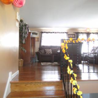 A cozy living room decorated with colorful streamers, featuring a set of stairs and sunlight streaming through the windows.