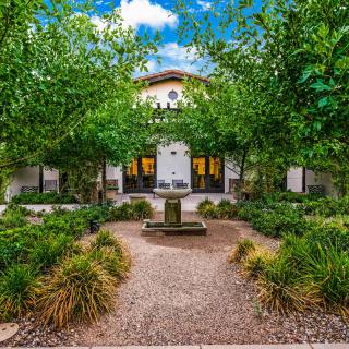 A serene courtyard garden with a central fountain, flanked by lush greenery and a charming building in the background.