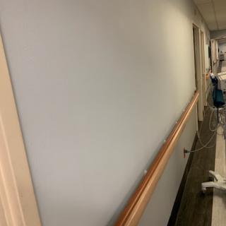 A view of a hallway featuring light-colored walls, a wooden handrail, and doors along the corridor.