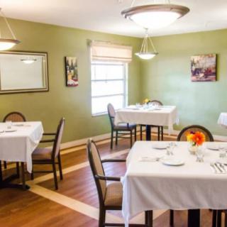 A cozy dining room with neatly arranged tables and chairs, featuring elegant tablecloths and warm lighting.