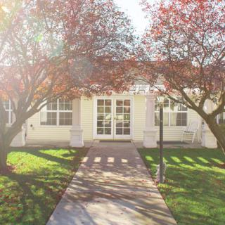 A sunny day view of a house with mature trees and a pathway leading to the entrance.