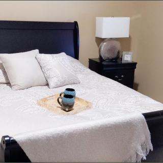 A neatly made bed with a tray and coffee cup on top, accompanied by pillows and a nearby nightstand with a lamp.