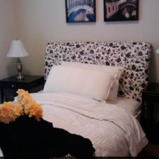 A cozy bedroom with a patterned headboard, flanked by lamps on bedside tables, and decorative flowers.