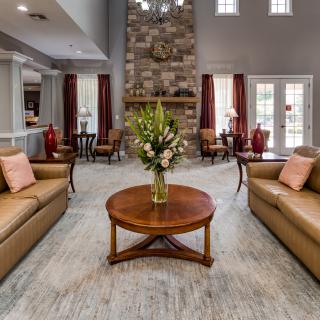 A cozy living room featuring a central coffee table with floral arrangements, surrounded by comfortable sofas and a stone fireplace.