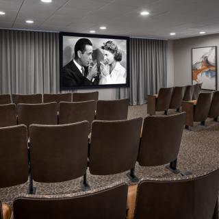 An empty theater room with a black and white movie playing on the screen.