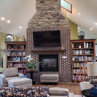 A cozy living room featuring a brick fireplace, surrounded by bookshelves, with comfortable seating arrangements.