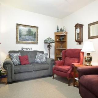 A cozy living room with a sofa, armchairs, a lamp, and decorative elements like a painting and clock.