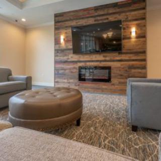 A modern living room with a cozy seating area, featuring a large TV and a fireplace set in wood paneling.