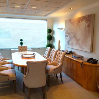 A modern conference room featuring a stylish dining table surrounded by upholstered chairs, complemented by decorative artwork and plants.