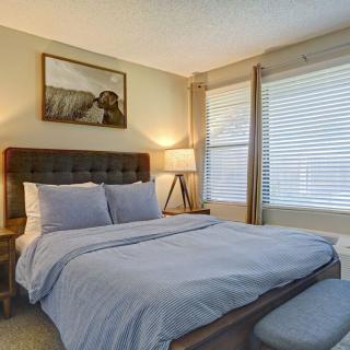 A cozy bedroom with a neatly made bed, soft lighting, and large windows.
