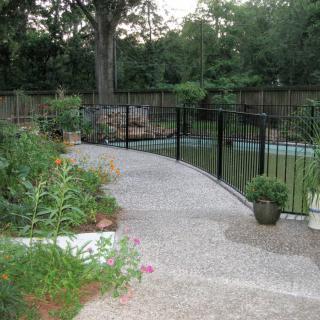 A garden pathway with plants and a black fence.