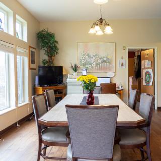 A cozy dining room with a large table and chairs, decorated with artwork, plants, and warm lighting.