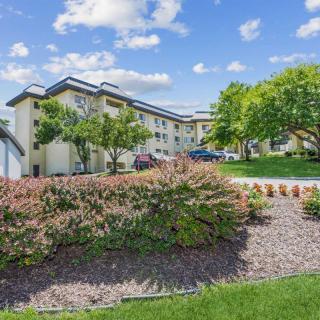 A scenic view of an apartment building surrounded by lush greenery and a partly cloudy sky.