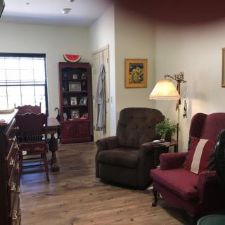 A cozy living room with armchairs and a bookshelf, illuminated by a standing lamp.