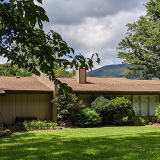 A serene suburban house surrounded by lush greenery and mountains in the background.