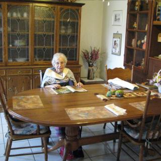 An elderly person sitting at a dining table in a cozy home setting, reading a magazine.