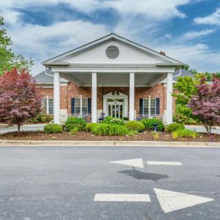 A traditional brick building with white columns at the entrance, surrounded by landscaped greenery and trees.