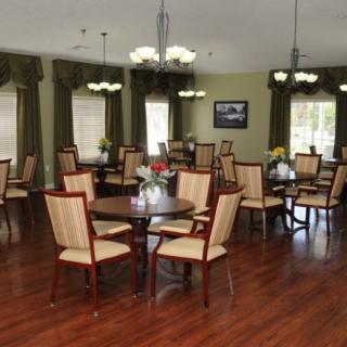 A well-lit dining room featuring wooden floors, multiple tables and chairs, with elegant chandeliers and curtains.