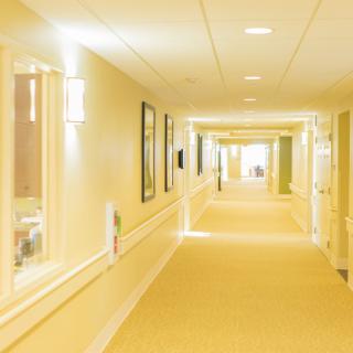 A well-lit, empty hallway with carpeted floors and framed pictures on the walls.