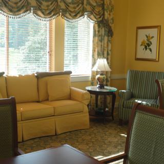 A cozy living room with yellow walls, featuring a sofa, armchair, and a table lamp by the window.