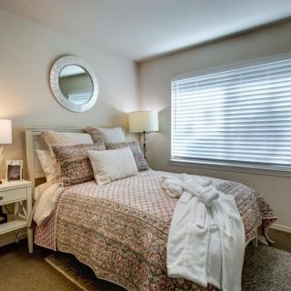 A cozy bedroom with patterned bedding, a wall mirror, and soft lighting.