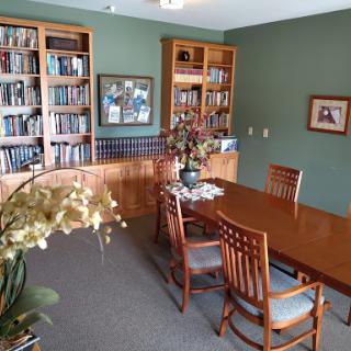 A cozy library and dining area featuring wooden bookshelves filled with books, a polished dining table surrounded by chairs, and decorative plants enhancing the space.