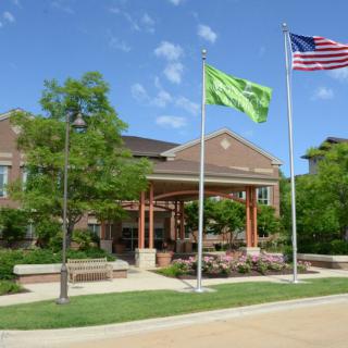 A building with two flags in front, surrounded by trees under a clear blue sky.
