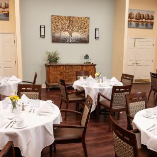 A cozy dining room with elegantly set tables and chairs, featuring tasteful decor.