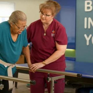 A healthcare professional assists an elderly woman during a physical therapy session.