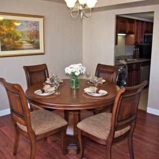 A cozy dining room with a round wooden table set for four, adorned with elegant place settings and a centerpiece of flowers.