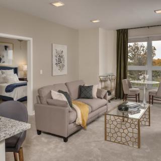 A modern apartment living room with a comfortable sofa, stylish artwork, and a view into the bedroom area.