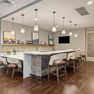 A modern kitchen interior with a long countertop, bar stools, and pendant lights.