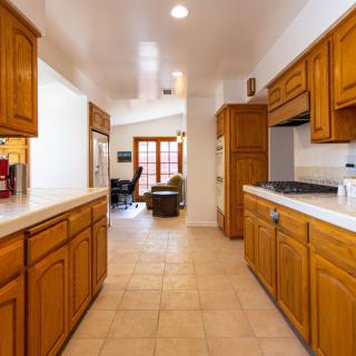 A modern kitchen with wooden cabinets and tile flooring, featuring bright lighting.
