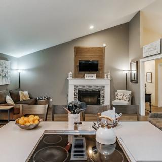 A modern living room with a kitchen island, cozy seating, and a fireplace under a vaulted ceiling.