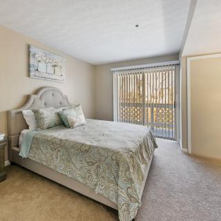 A cozy bedroom with a bed, side table, and a window with blinds.