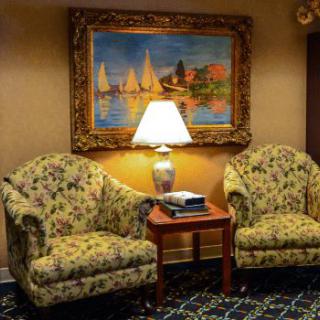 A cozy living room setup with two floral-patterned chairs, a lamp on a side table, and a colorful painting of sailboats hanging on the wall.
