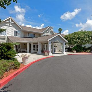 A suburban building with a driveway and landscaped surroundings under a blue sky.